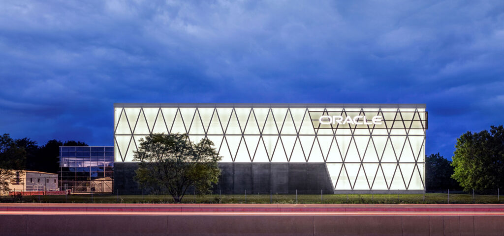 Exterior view of Oracle Industries Innovation Lab in Deerfield, Illinois, featuring a fully illuminated glass façade with triangular structural geometry that creates a striking nighttime architectural presence.